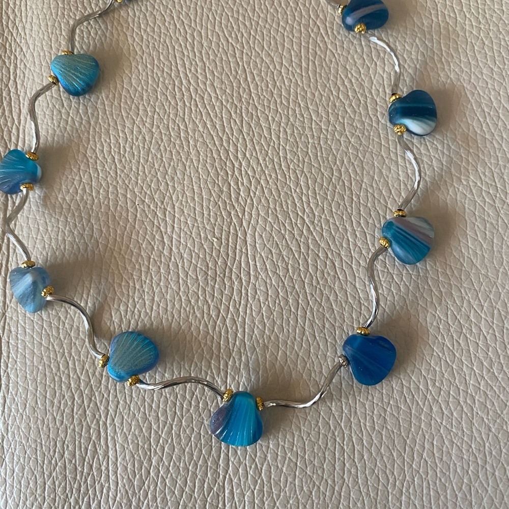 Necklace features blue shells in various shades of blue. Silver spacers. 16 in